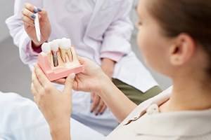 Dentist pointing with pen to model of dental implant held by patient