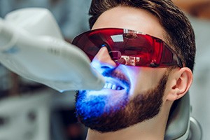 Man in protective goggles in dental chair with UV light applied to teeth whitening