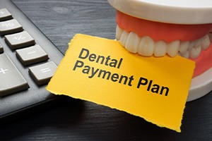Artificial teeth next to calculator biting a yellow paper that says “Dental Payment Plan”