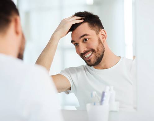 Patient in Randolph smiling in mirror after gum recontouring results