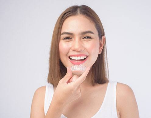 Woman with brown hair smiling while holding Invisalign