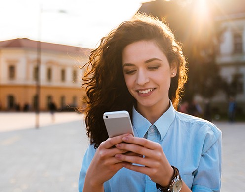 Smiling woman looking at cellphone as she schedules T M J therapy