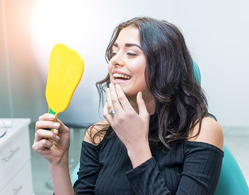 Smiling woman looking in dental mirror