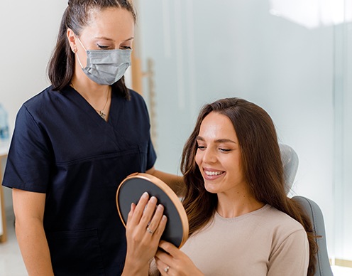 Patient smiling at reflection in mirror with dental assistant