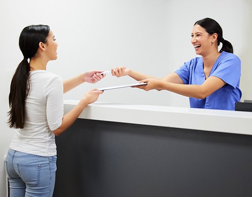Smiling dental assistant handing patient form