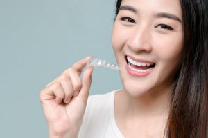 a young woman smiling while holding an Invisalign clear aligner 
