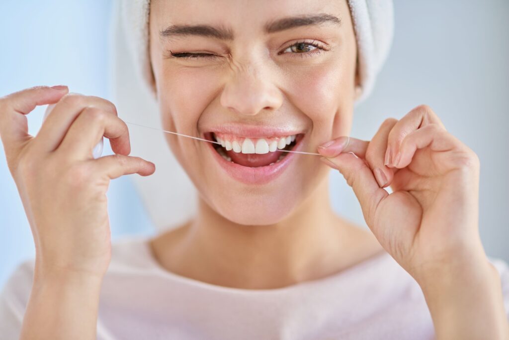Woman with towel on hair winking and flossing